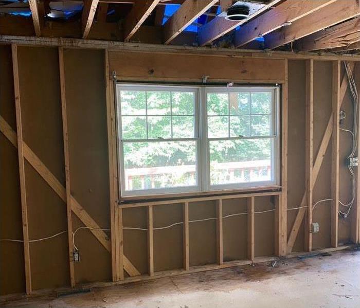 A double window set looking out to green trees. Surrounded by wooden beams on the wall and ceiling. Flooring is cement.