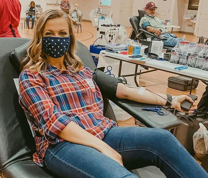 white female with blond hair, plaid shirt, and jeans giving blood 