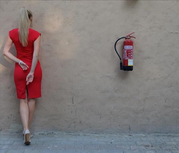 A Woman stands next to a wall beside a fire extinguisher